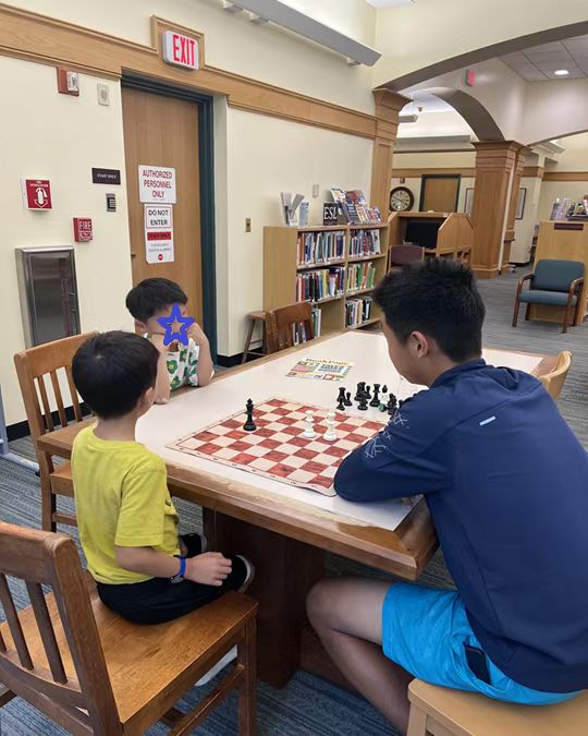 A student volunteer and children seated around a chessboard