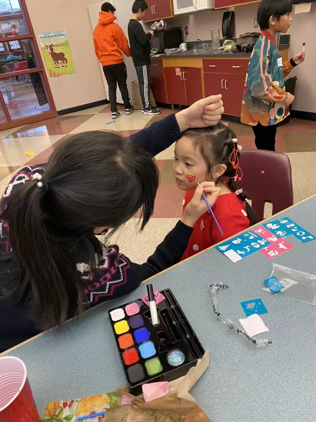 A volunteer painting a strawberry design on a child’s cheek