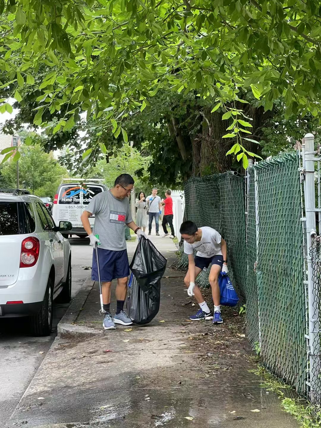 Two volunteers picking up litter beside a neighborhood fence